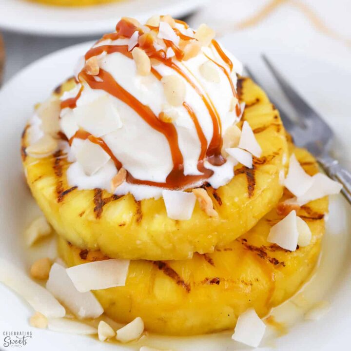 Image of two rings of grilled pineapple topped with a scoop of ice cream, drizzled with sauce and nuts.