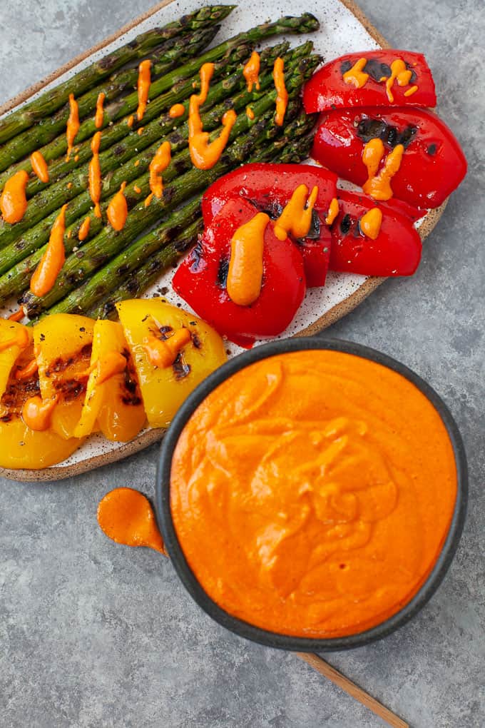 Image of romesco sauce in bowl with grilled vegetables garnished with same sauce.