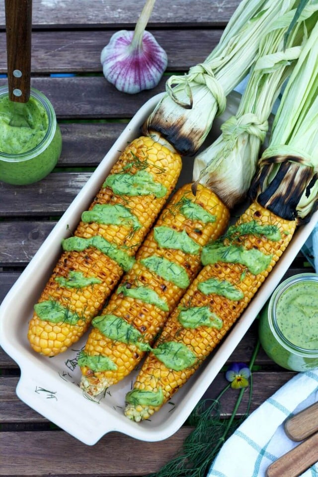 Image of three grilled corn on the cob in a dish with dressing.