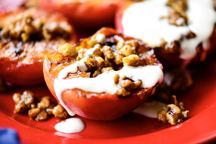 Image of grilled peaches with nuts and cream.on red plate.