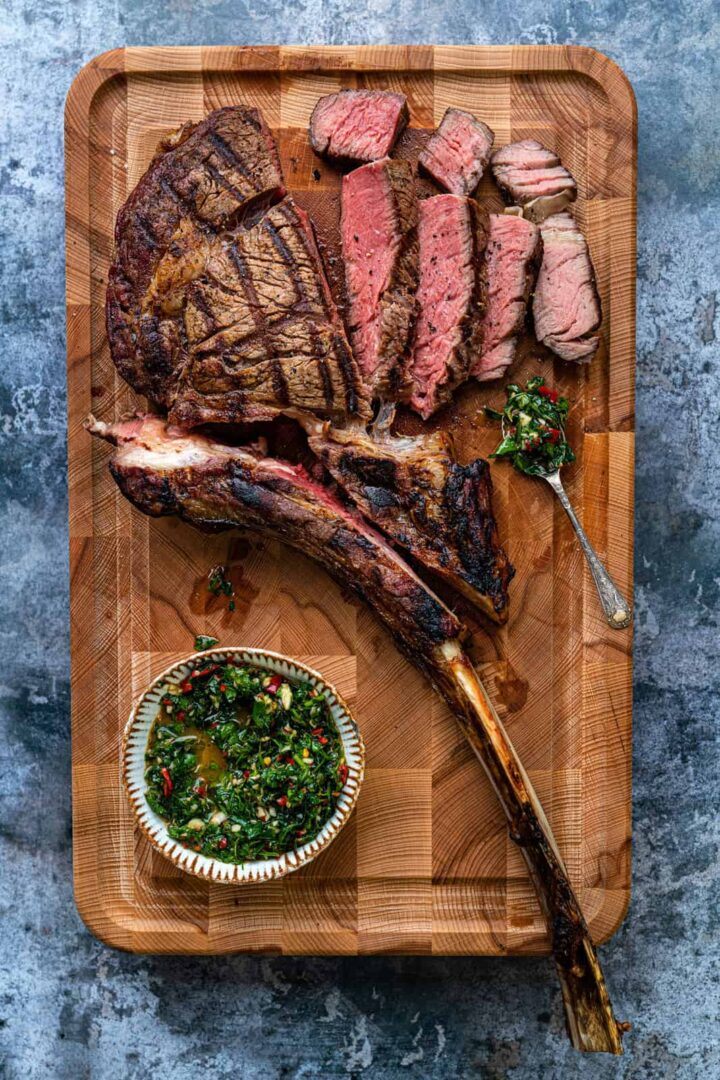 Image of tomahawk steak sliced on wooden board.