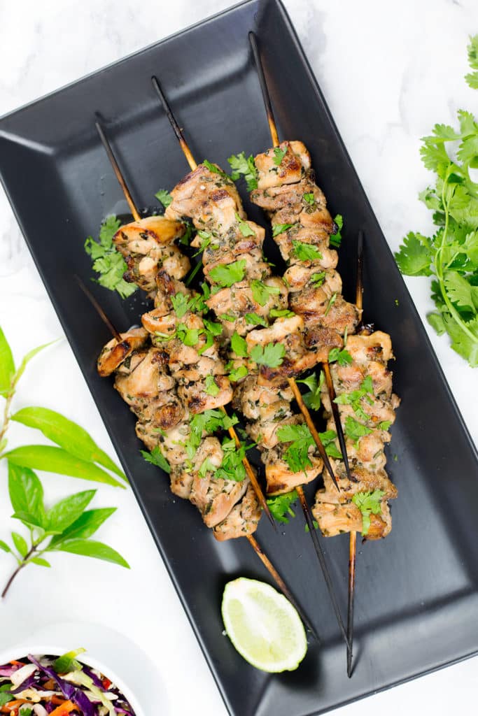 Image of six chicken skewers on black platter with lime.