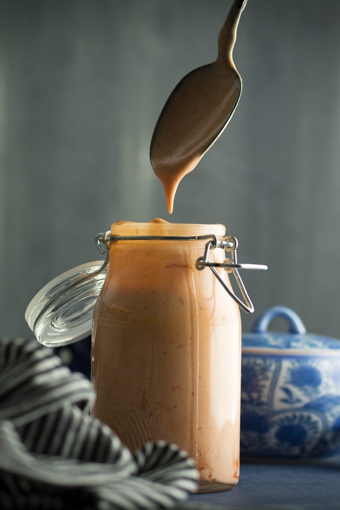 Image of spoon dripping with boom boom sauce over jar of same sauce.