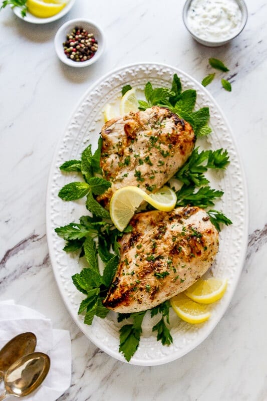 Image of grilled chicken breast with fresh herbs on white platter overhead view.