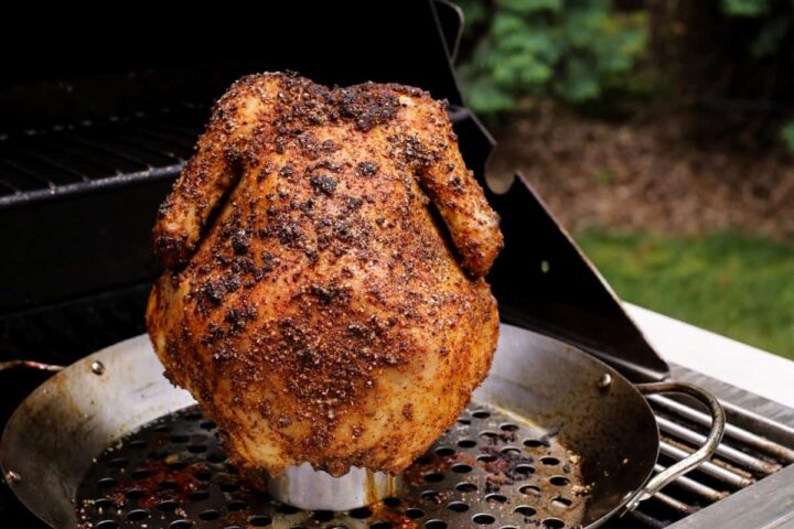 Image of grilled whole chicken on beer can on the grill.