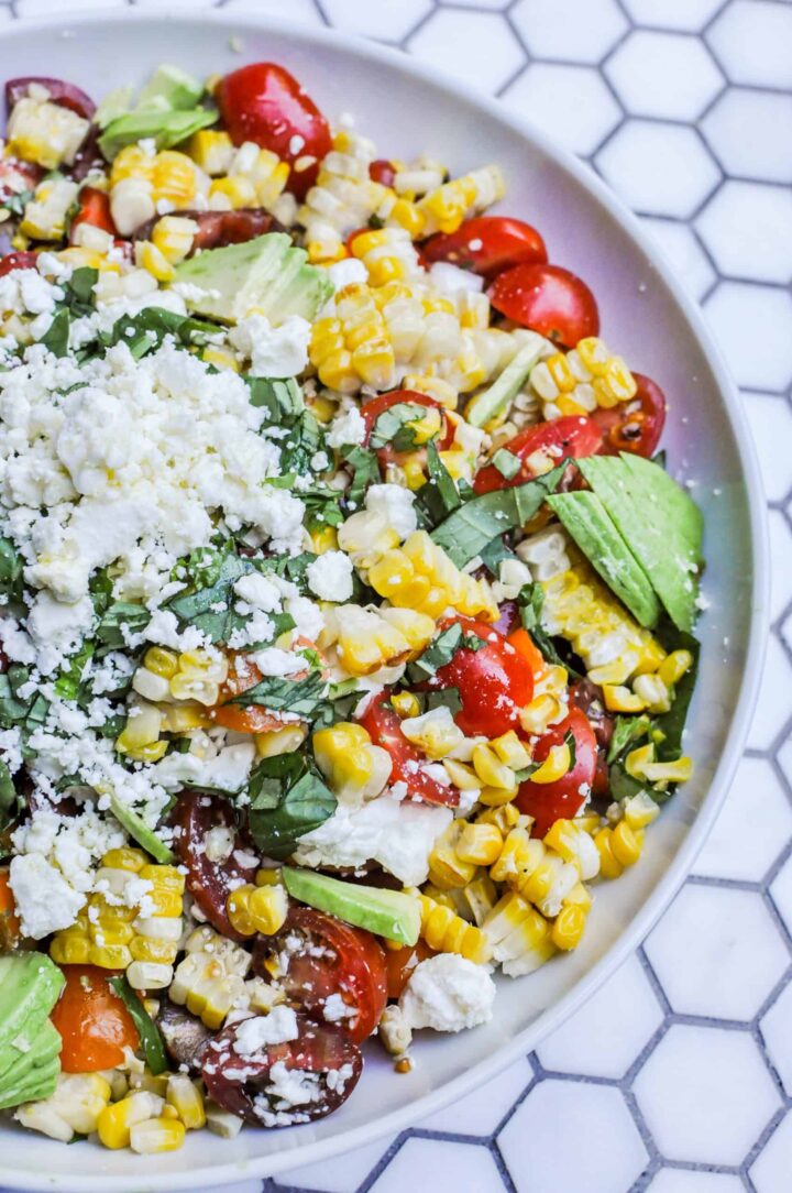Image of grilled corn salad with cheese and herbs on white plate.