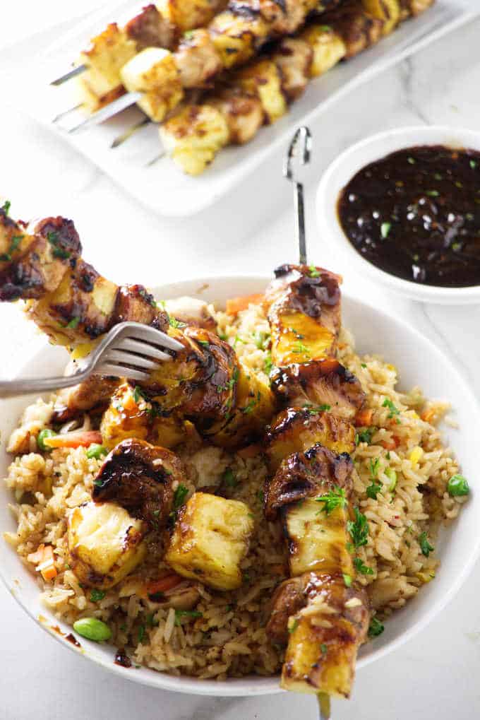 Image of chicken and pineapple skewers over vegetable rice in a large white bowl.
