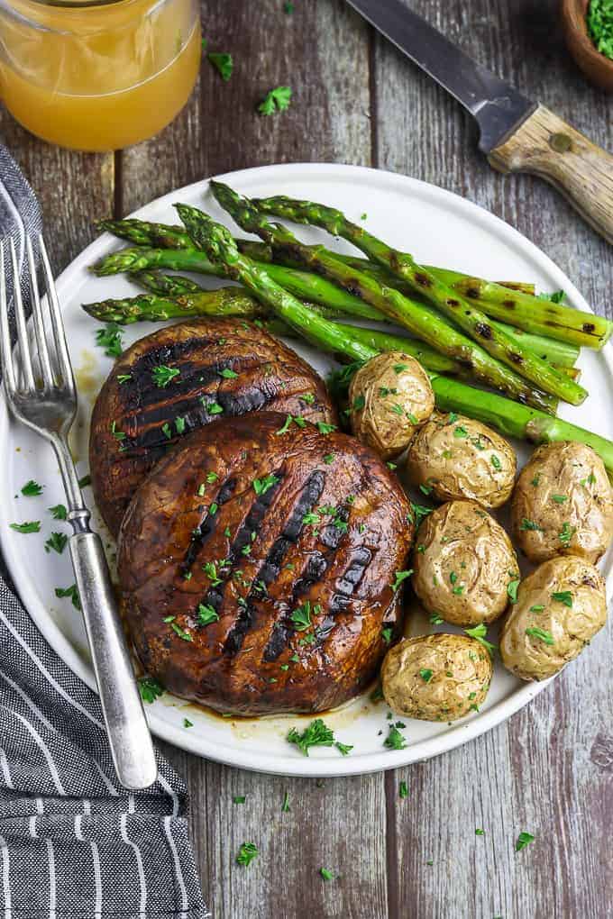 Image of two grilled portobello mushrooms on plate with asparagus and potatoes.