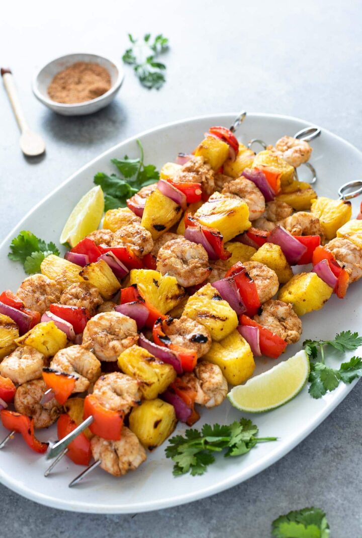 Image of grilled jerk shrimp and pineapple skewers on white platter.