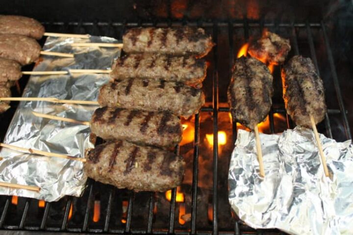 Image of kebabs on wooden skewers cooking on grill.