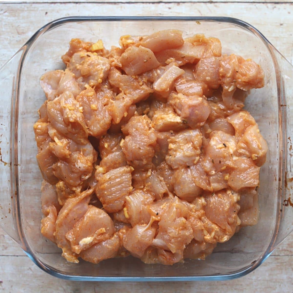 Raw chicken marinating in a glass bowl.