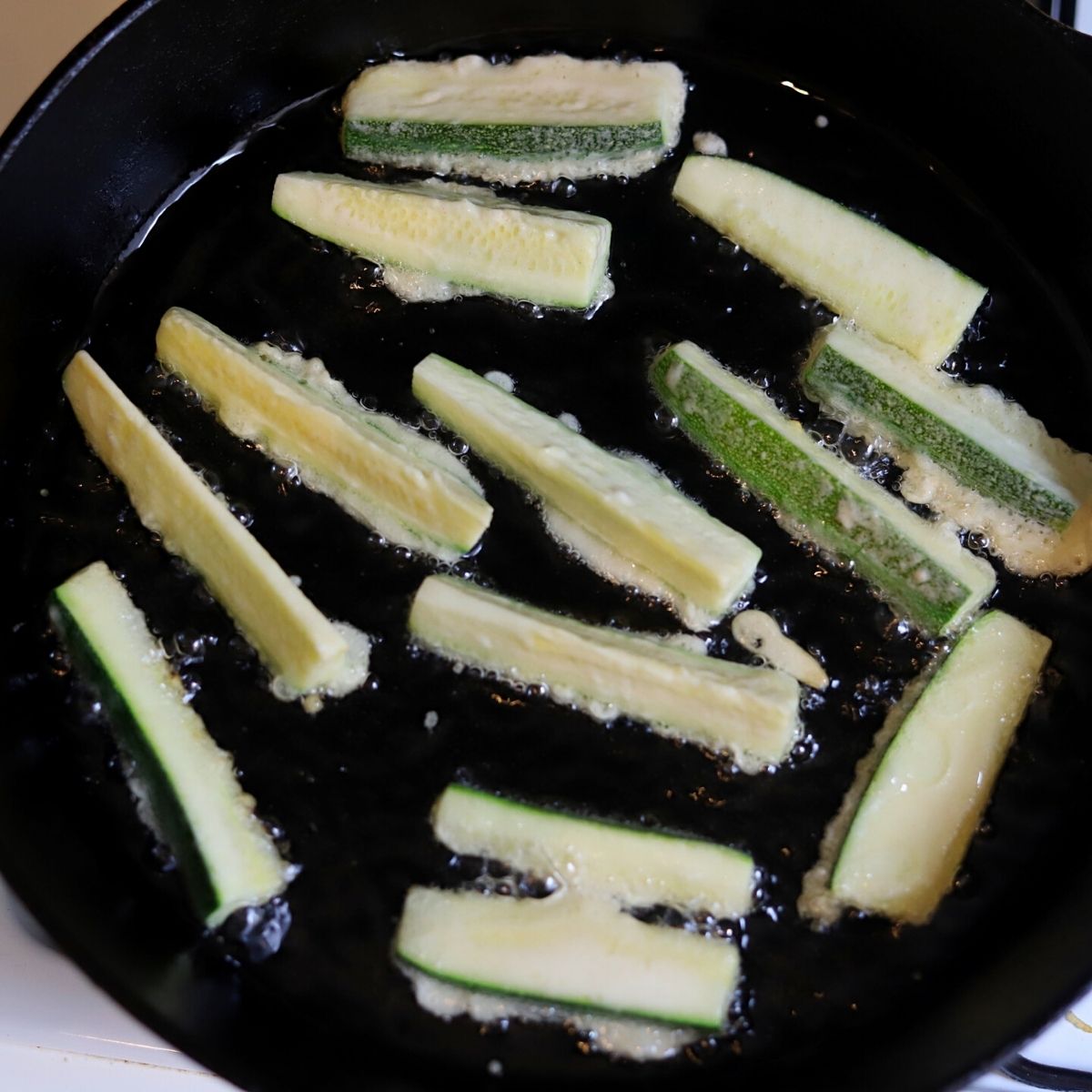 Frying battered zucchini in an iron skillet.