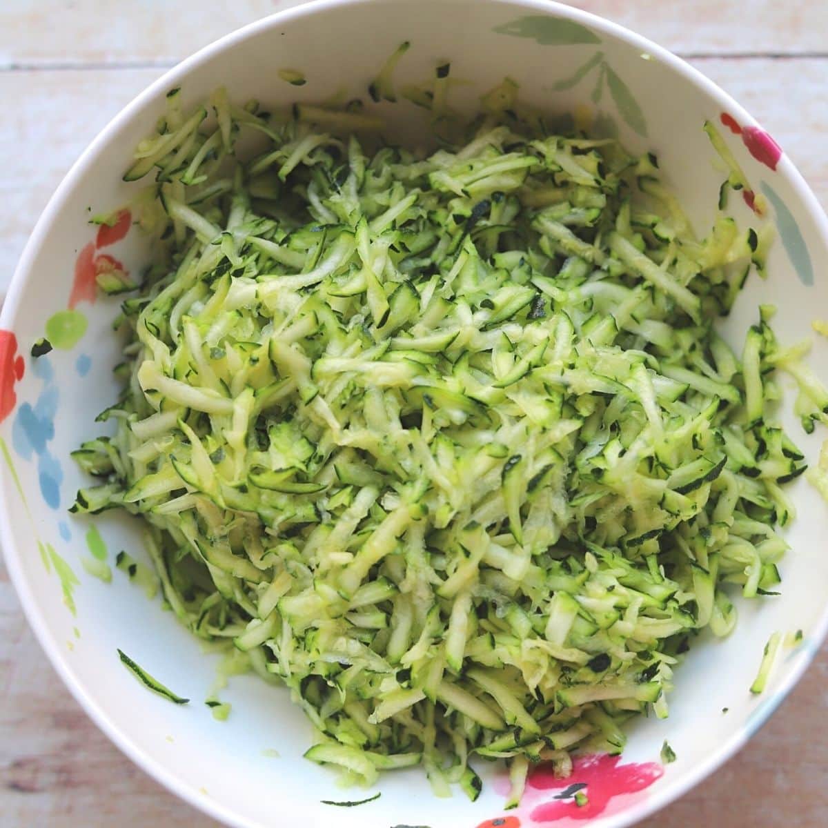 White painted bowl full of grated zucchini.