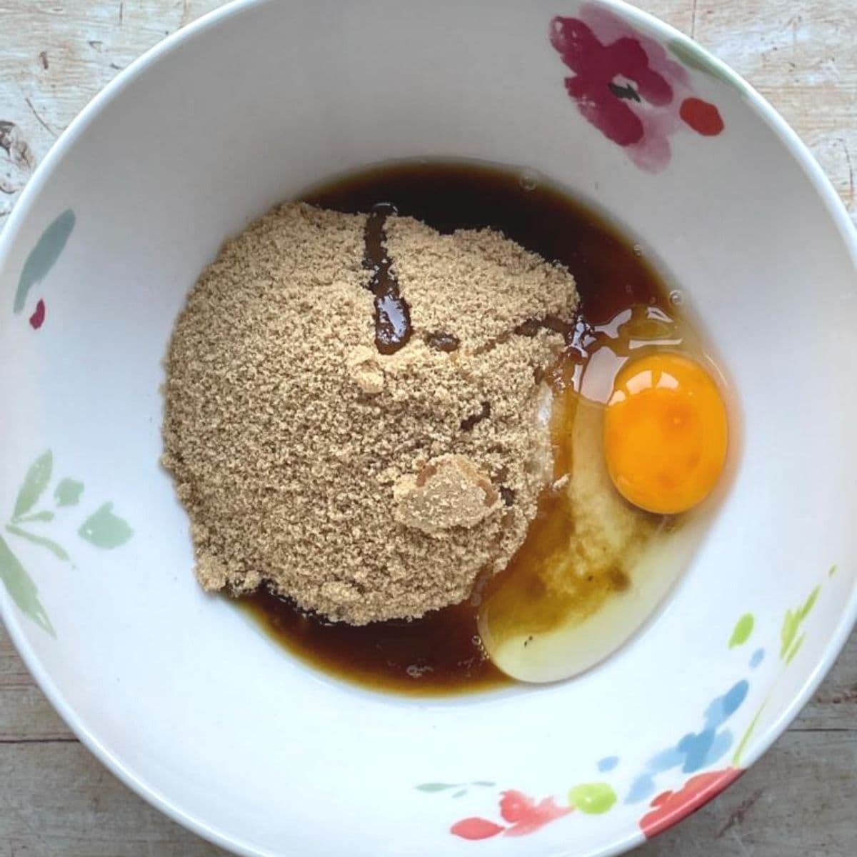 Egg, butter, vanilla and sugars in a white painted bowl.