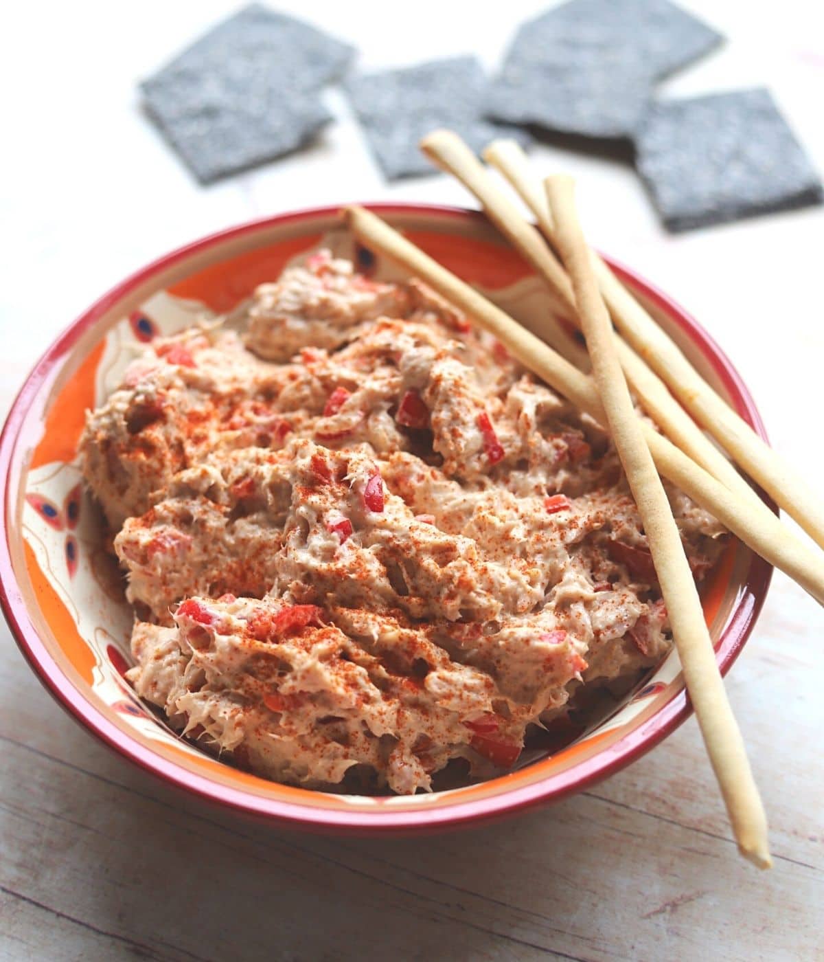 Tuna mix in a bowl with breadsticks and crackers.