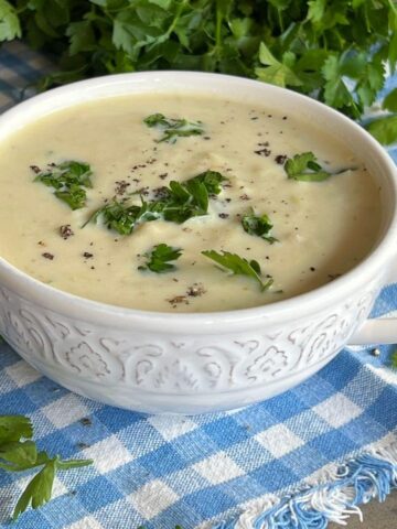 A white bowl containing Scottish smocked haddock soup topped with fresh parsley and parsley in the background.