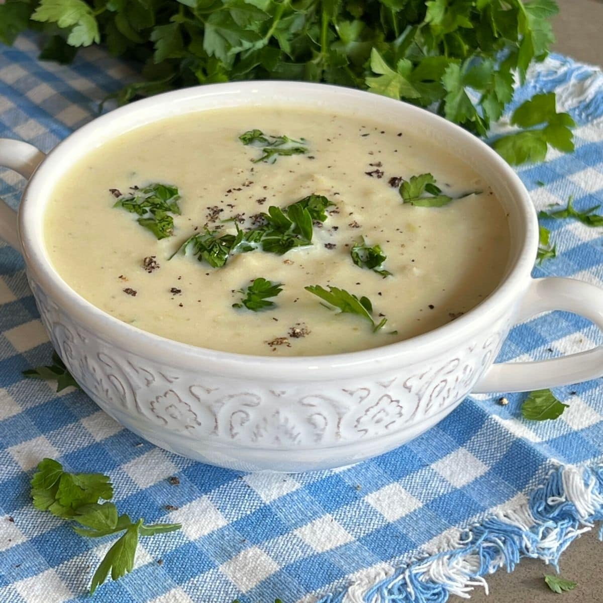 A white bowl containing Scottish smocked haddock soup topped with fresh parsley and parsley in the background.