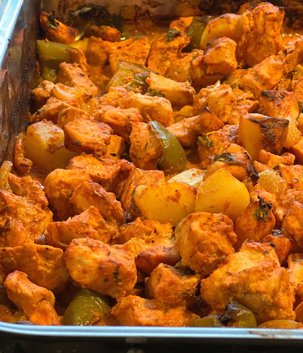 Baked spicy chicken and vegetables in roasting pan.