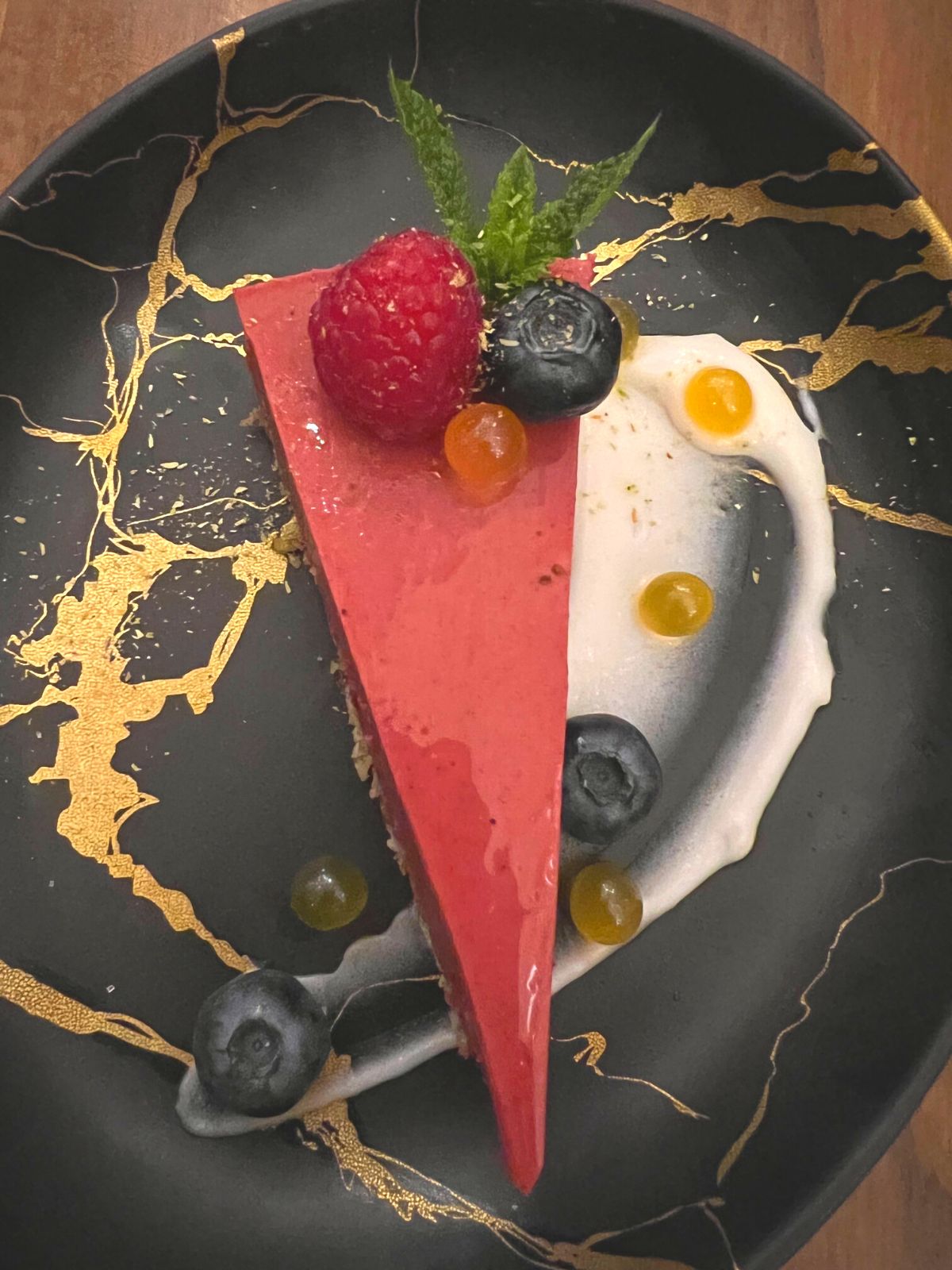 Slice of Raspberry tart with berries on black and gold plate.