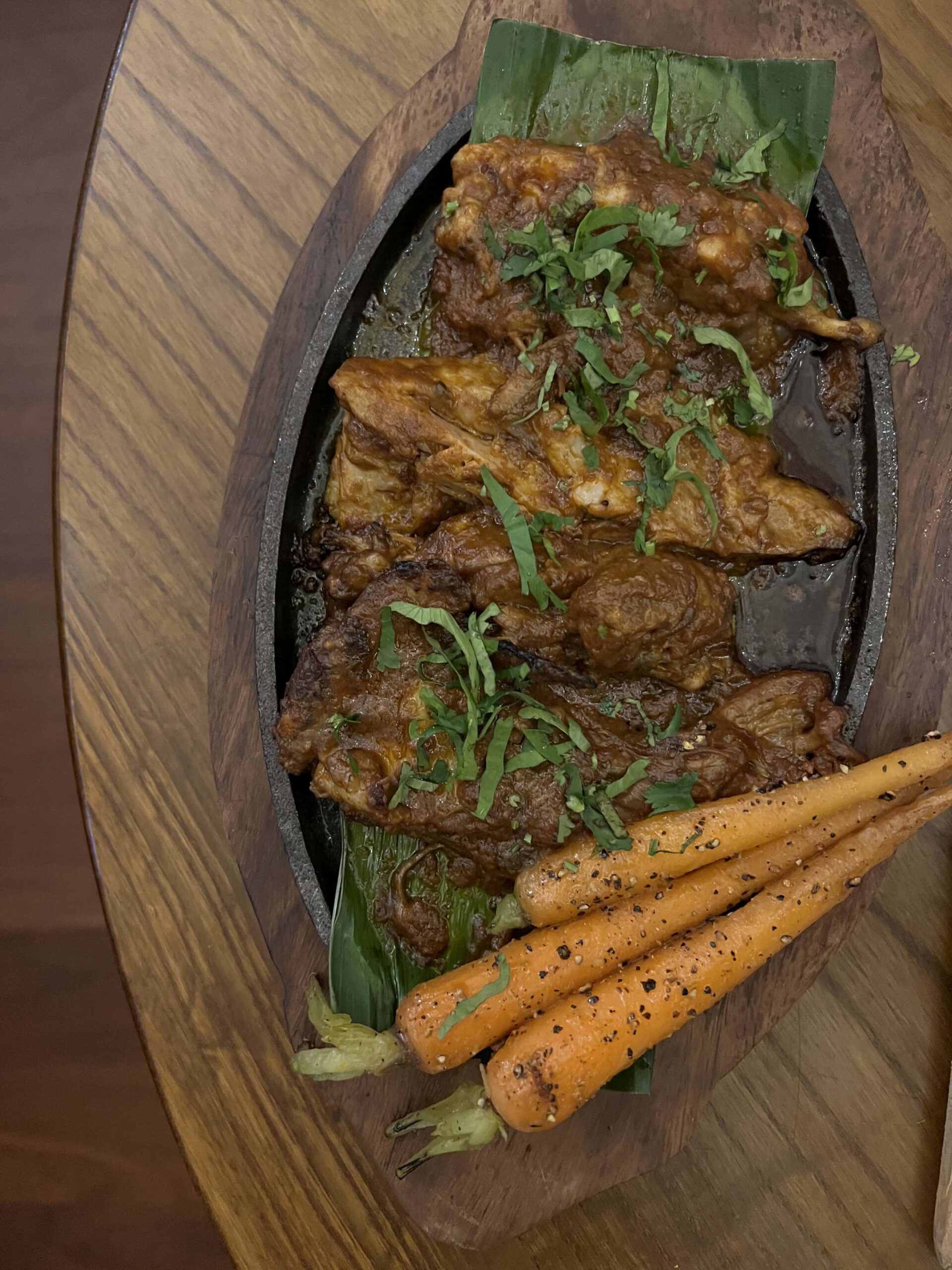 Goat curry with carrots on wooden sizzler serving dish.