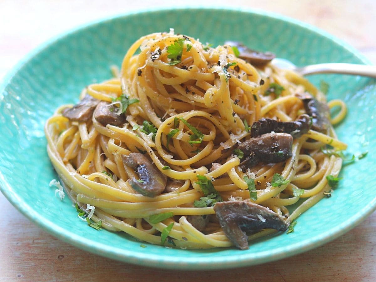 Spaghetti with gorgonzola sauce and sliced mushrooms in blue bowl.