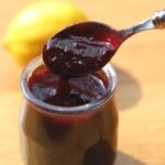 Cherry sauce in glass jar with spoon.