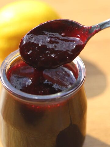 Cherry sauce in glass jar with spoon.