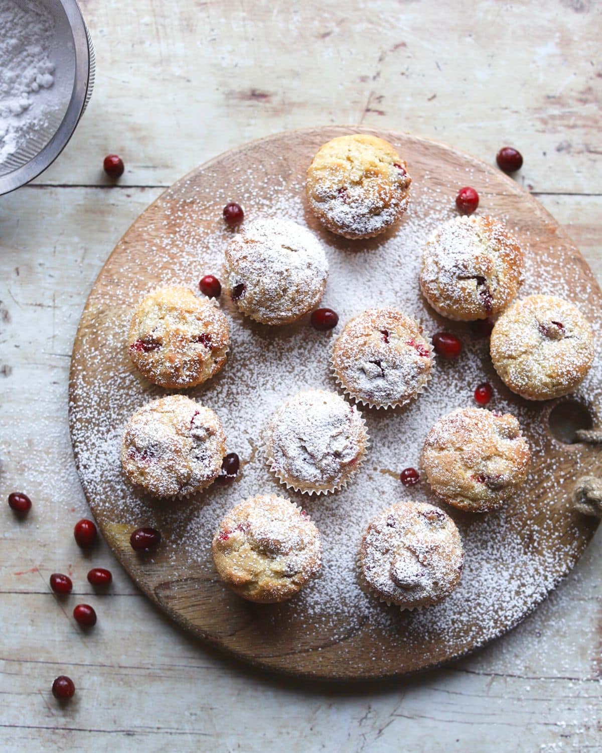 Cranberry muffins on wooden tray dusted with powdered sugar seen from above.