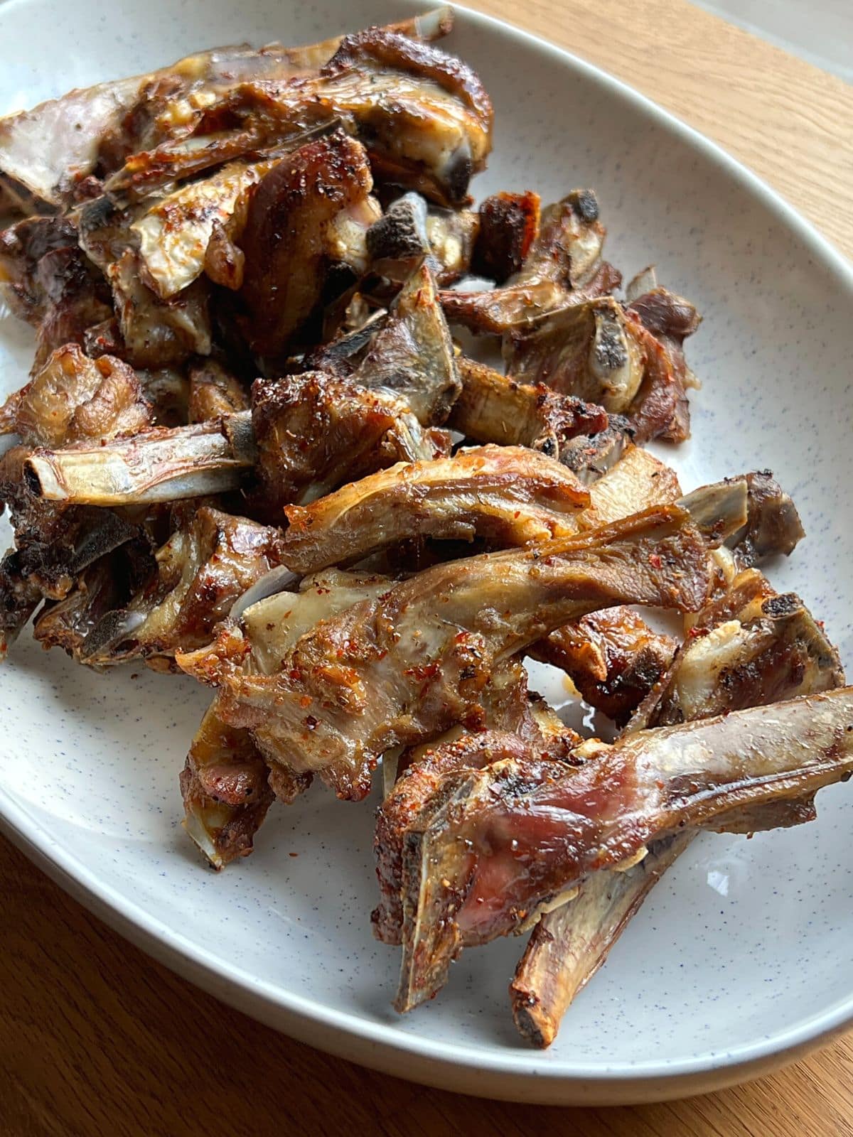 Close up of roasted lamb ribs on a white dish.