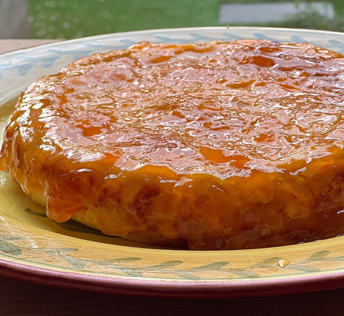 Orange cake covered in apricot glaze on yellow plate.