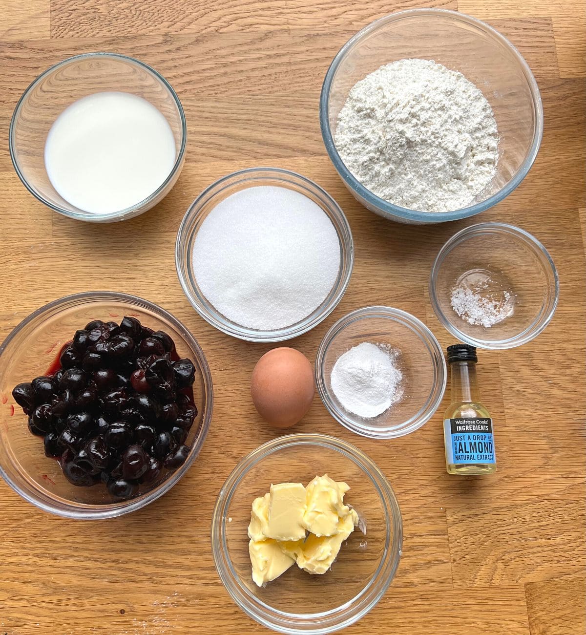 Small bowls of cherry muffin ingredients on a wooden counter.