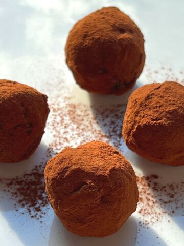 Four chocolate bliss balls on a white plate.