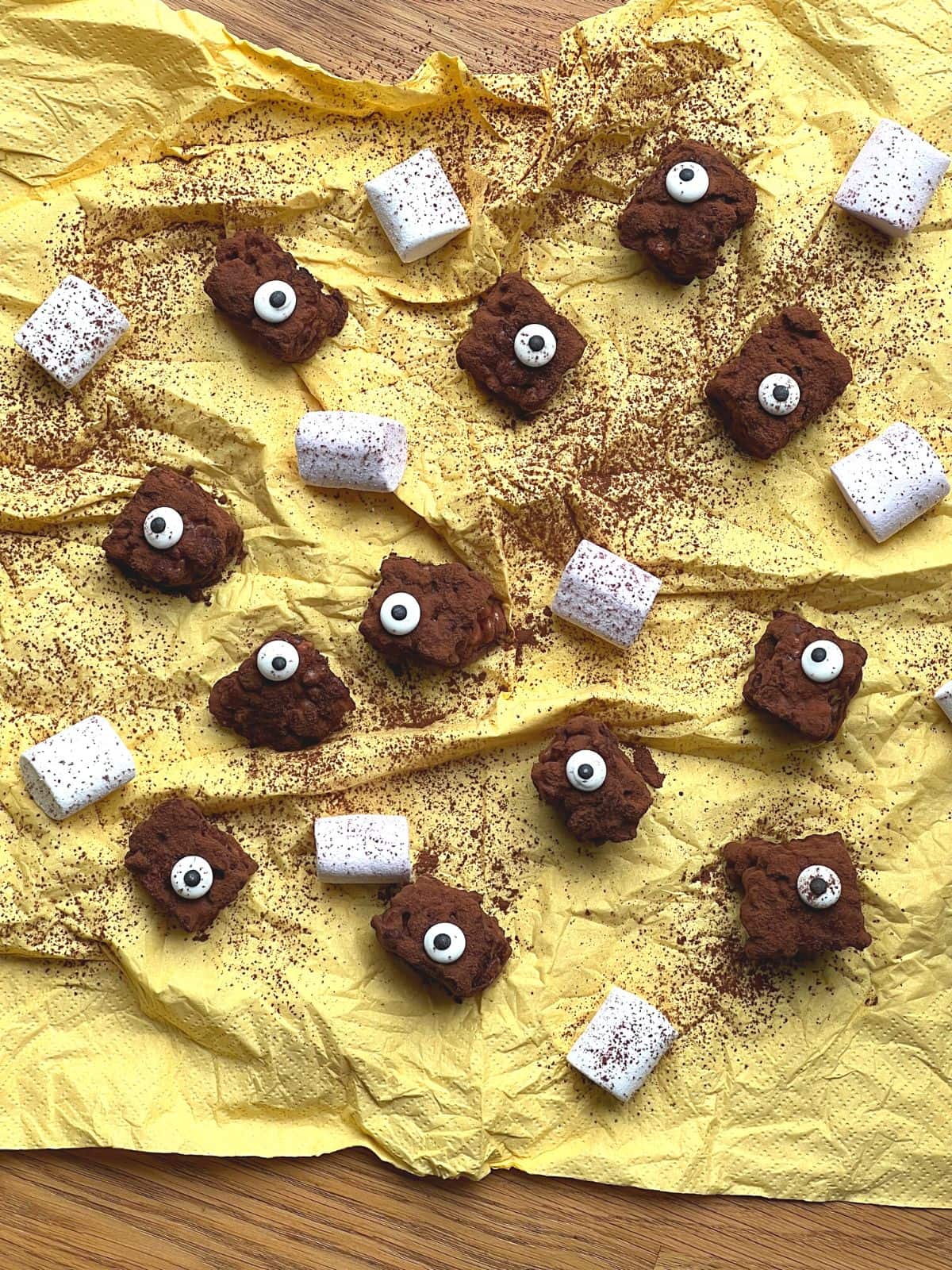 Chocolate rice krispie squares with candy eyes on yellow tissue paper with white marshmallows.