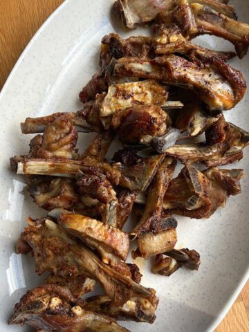 Close up of roasted lamb ribs on white platter.