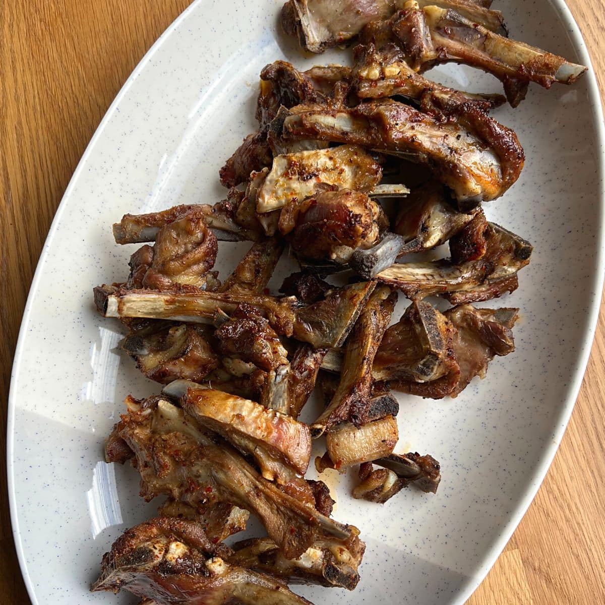 Close up of roasted lamb ribs on white platter.