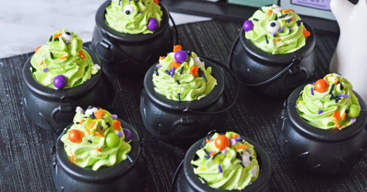 Seven plastic black cauldrons filled with green pudding topped with candy.
