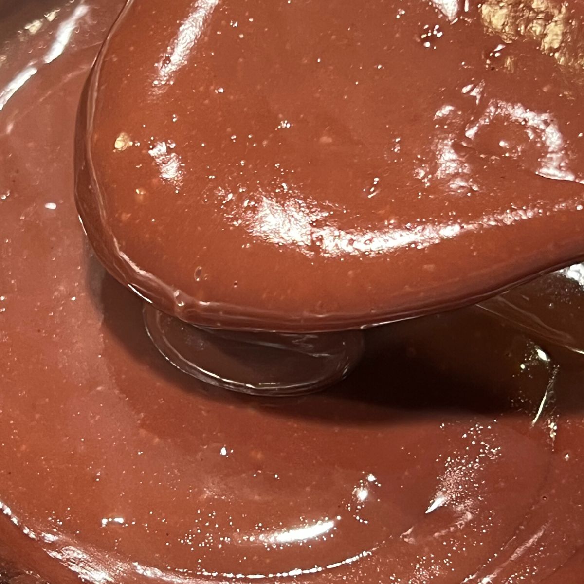 Smooth chocolate pudding on wooden spoon in saucepan.