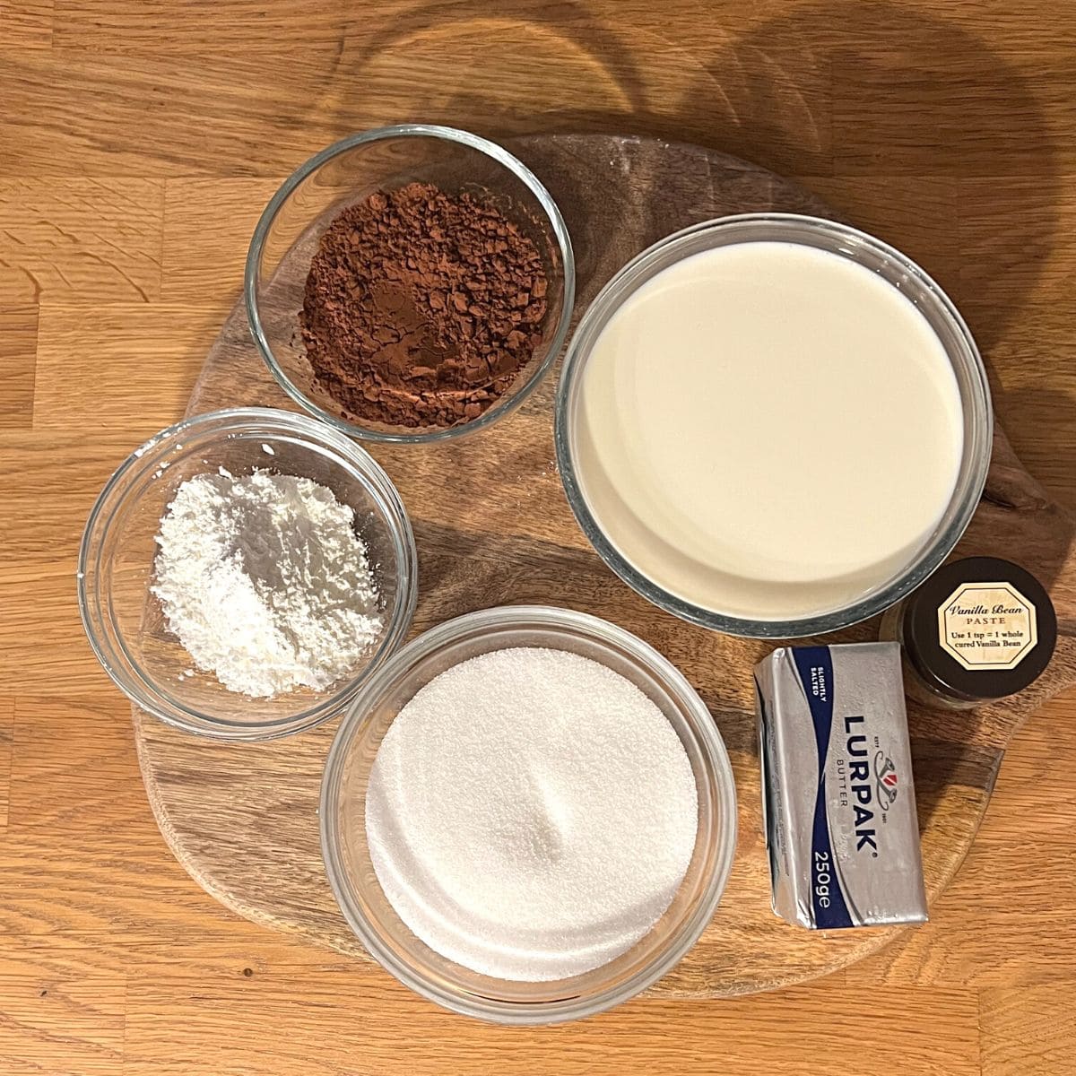Chocolate pudding ingredients in small bowls on wooden counter.