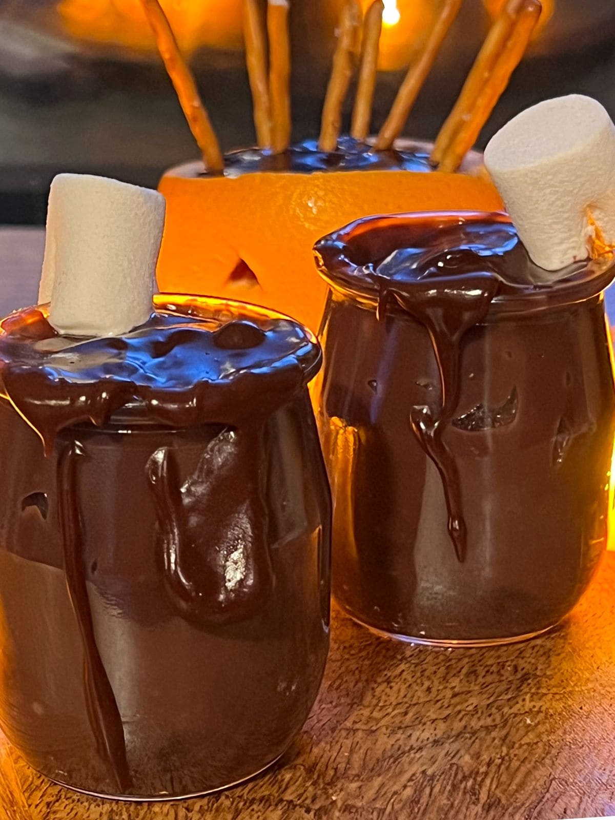 Two cups of chocolate pudding with marshmallow next to orange jack-o-lantern.