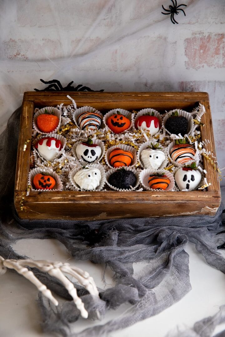 Wooden box containing halloween decorated strawberries.