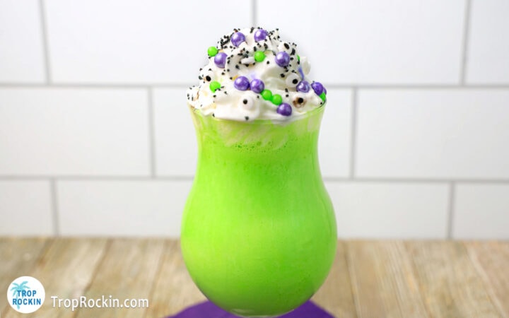 Glass of green milkshake topped with whipped cream and small coloured balls.