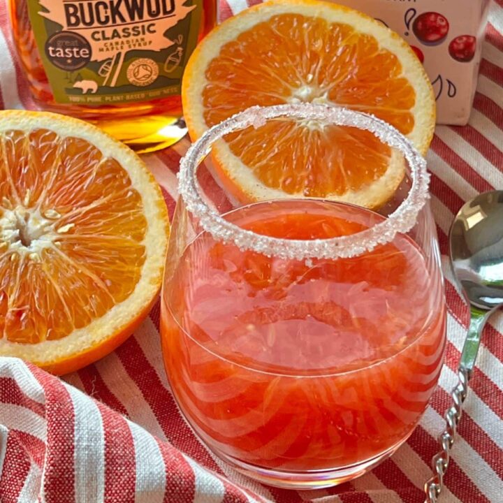 Orange drink next to halved oranges on red stripe cloth.