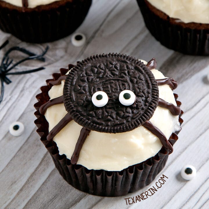 Cupcake decorated like a spider with oreo and candy eyes on white frosting.