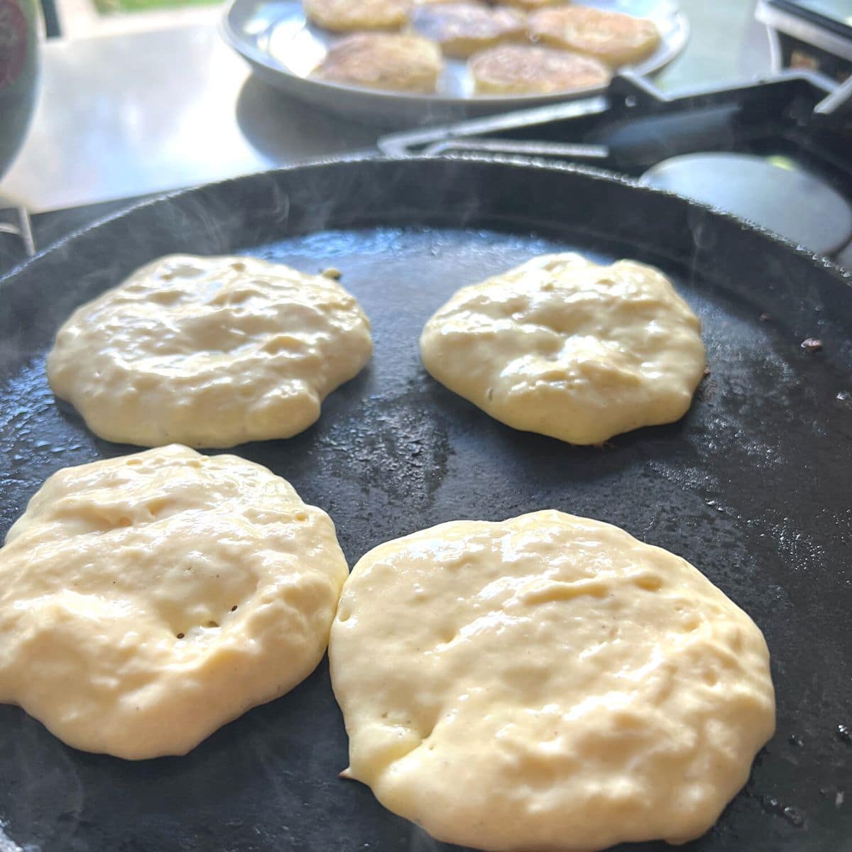 Four pancakes cooking on iron skillet.