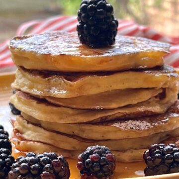 Stacked pancakes with blackberries on yellow plate.