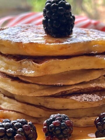 Stacked pancakes with blackberries on yellow plate.