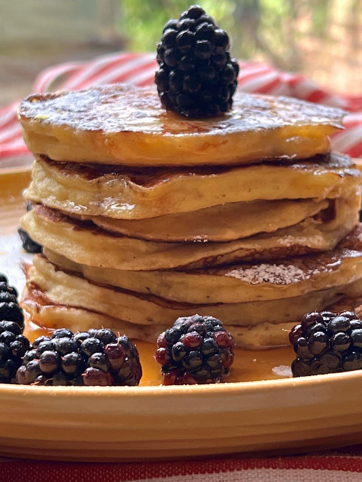 Stacked pancakes seen from side on yellow plate with blackberries.