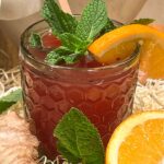 Apple cider vinegar drink in green glass with orange slice and mint.