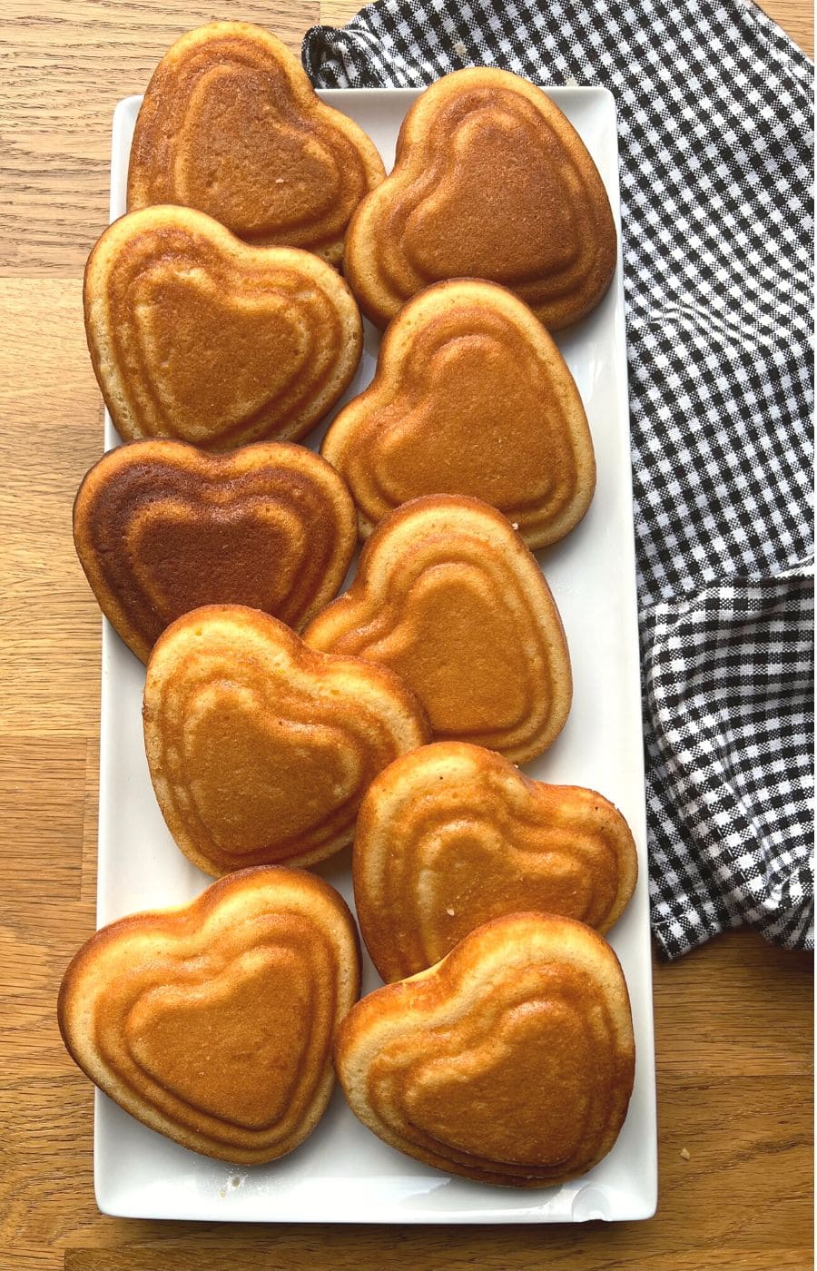 Cooled mini heart cakes on white plate with teatowel.