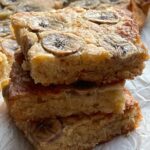 Three stacked banana blondies on baking paper.